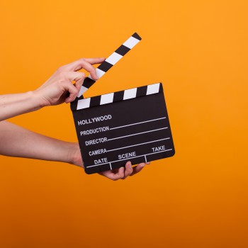 woman holding professional film slate, movie clapper board in studio over yellow background. Hollywood production objects concept