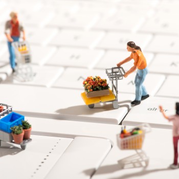 Miniature people shopping for various items with carts on a white computer keyboard in a concept of online shopping with focus to a man in the center